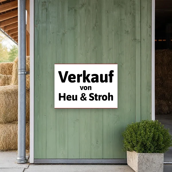 Querformat-Schild am Hofeingang für den Verkauf von Heu und Stroh, gut sichtbar an einer weißen Wand montiert