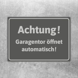 Grauer Aufkleber mit dem Hinweis Achtung Garagentor öffnet automatisch für die Zufahrt.