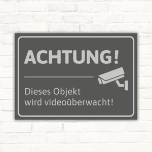 Schild mit dem Hinweis „Achtung! Dieses Objekt wird videoüberwacht“ und Kamerasymbol.