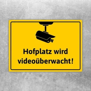 Gelber Aufkleber mit Kamera-Symbol und dem Hinweis: Hofplatz wird videoüberwacht.