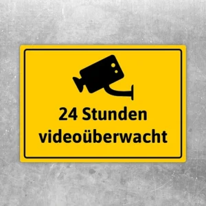 Gelber Aufkleber mit Kamerasymbol und dem Text 24 Stunden videoüberwacht.