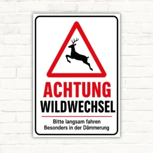 Achtung Wildwechsel Warnschild mit Hirsch im Warndreieck und dem Text 'Bitte langsam fahren' auf weißem Schild.