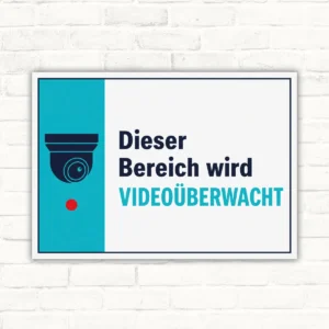 Videoüberwachung Schild mit Kamera-Symbol und Text „Dieser Bereich wird videoüberwacht“ auf weiß-türkisem Hintergrund.