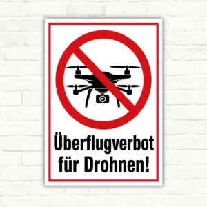 Schild mit rotem Verbotssymbol und Drohne, darunter der Text „Überflugverbot für Drohnen!“ als Verbotsschild.