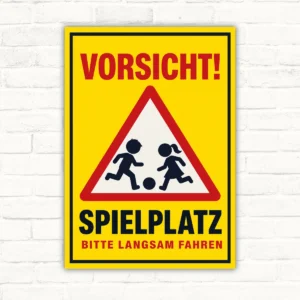 Vorsicht Spielplatz Schild mit roter Warnschrift und Kindern im Dreieck, Hinweis: Bitte langsam fahren, auf gelber Alu-Verbundplatte.