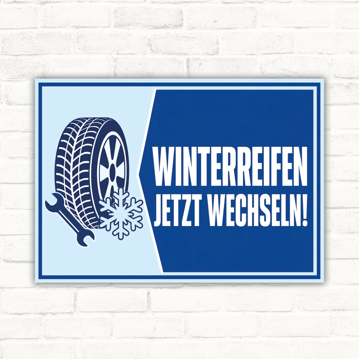 Bedrucktes Hinweisschild mit Reifenmotiv und dem Text „WINTERREIFEN JETZT WECHSELN!“ auf blauem Hintergrund.