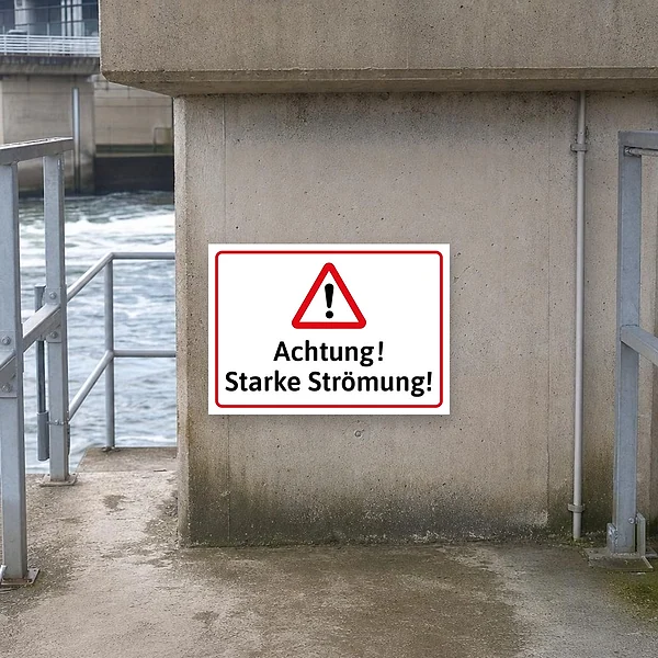 Warnschild an einem Fluss- oder Uferbereich, das Besucher vor starker Strömung am Wasser warnt