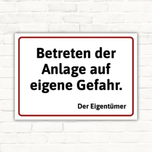 Schild mit dem Text „Betreten der Anlage auf eigene Gefahr. Der Eigentümer“ in schwarzer Schrift mit rotem Rahmen auf weißem Hintergrund.