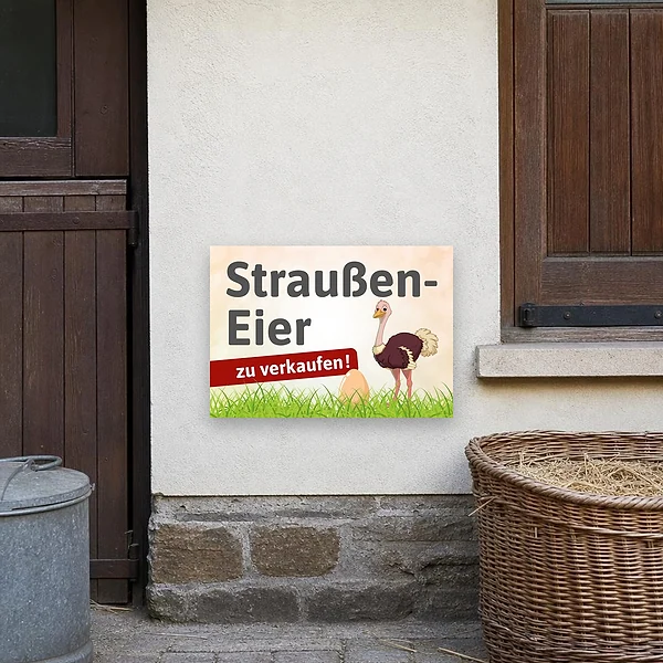 Ein Verkaufsschild für einen Hofladen mit der Aufschrift Straußen-Eier zu verkaufen, platziert im Außenbereich an einer Wand