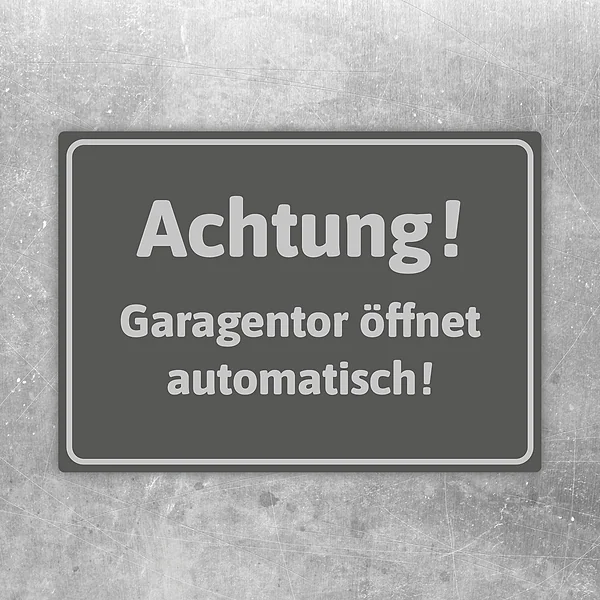 Grauer Aufkleber mit dem Hinweis Achtung Garagentor öffnet automatisch für die Zufahrt.