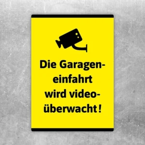 Gelber Aufkleber mit Kamerasymbol und Hinweis, dass die Garageneinfahrt videoüberwacht wird.