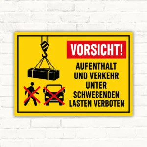 Warnschild mit Kranlast und Text „Vorsicht! Aufenthalt und Verkehr unter schwebenden Lasten verboten“ auf gelbem Hintergrund.