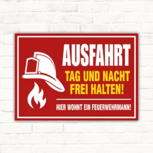 Ausfahrt frei halten Schild mit Feuerwehrhelm und Flammensymbol, rotem Hintergrund und dem Text Tag und Nacht frei halten.