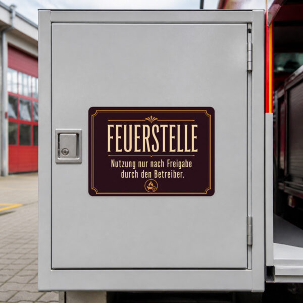 KI-generiertes Anwendungsbeispiel: Feuerstelle Aufkleber mit Betreiberfreigabe-Hinweis auf dunkler Fläche im Außenbereich.