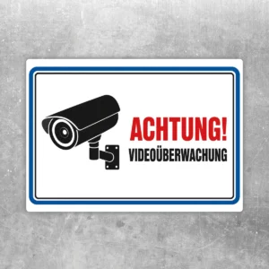 Querformat-Aufkleber mit Kamera-Symbol und Text „Achtung! Videoüberwachung“ in Rot, Schwarz, Weiß und Blau.