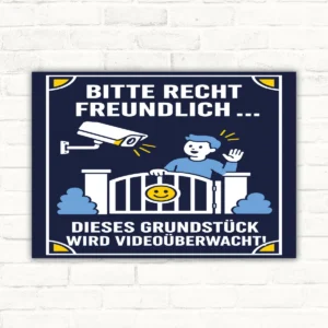 Videoüberwachungsschild im Hochformat mit Text „Bitte recht freundlich... Dieses Grundstück wird videoüberwacht!“ und Kameramotiv.