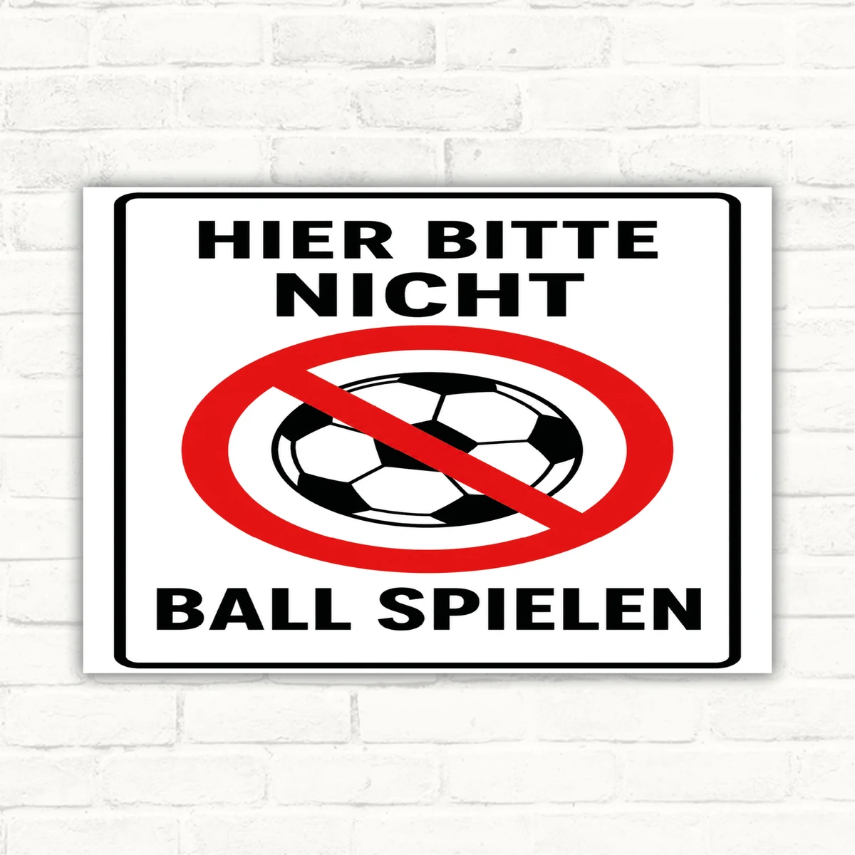 Hier bitte nicht Ball spielen Schild mit rotem Verbotssymbol und schwarzem Text auf weißem Hintergrund als Hinweisschild.