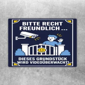 Videoüberwachungsschild Grundstück bitte recht freundlich Aufkleber mit Kamera, Tor und freundlicher Figur in Blau, Weiß und Gelb.