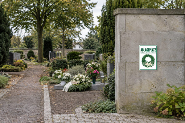 KI-generiertes Anwendungsbeispiel: Ablageplatz für Kränze, Gestecke und Blumen Schild – Hochformat passend auf einem Friedhof angebracht.
