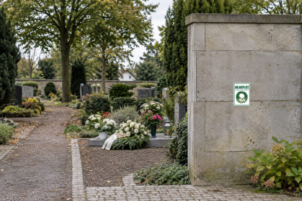 KI-generiertes Anwendungsbeispiel: Ablageplatz für Kränze, Gestecke und Blumen Aufkleber – Hochformat passend auf einem Friedhof angebracht.