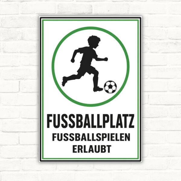 Fussballplatz Schild mit Spieler und Ball sowie dem Text „Fussballspielen erlaubt“ auf weiß-grünem Hintergrund.